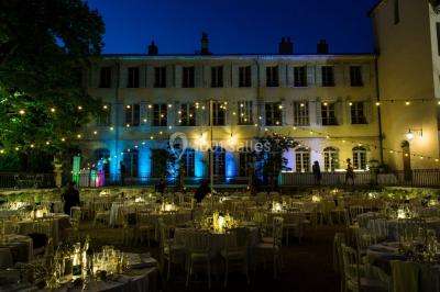 Allée bordée de palmiers éclairés, menant à une fontaine illuminée dans un jardin au crépuscule.