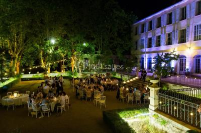 Allée bordée de palmiers éclairés, menant à une fontaine illuminée dans un jardin au crépuscule.