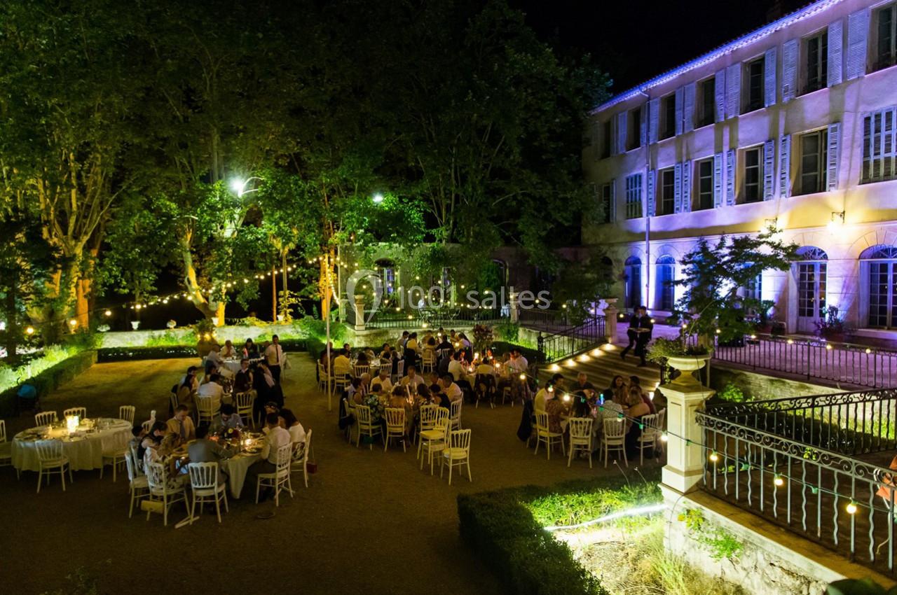 Personnes dînant en plein air dans un jardin éclairé, près d'un bâtiment ancien illuminé de nuit.