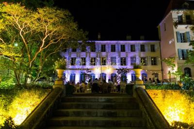 Allée bordée de palmiers éclairés, menant à une fontaine illuminée dans un jardin au crépuscule.