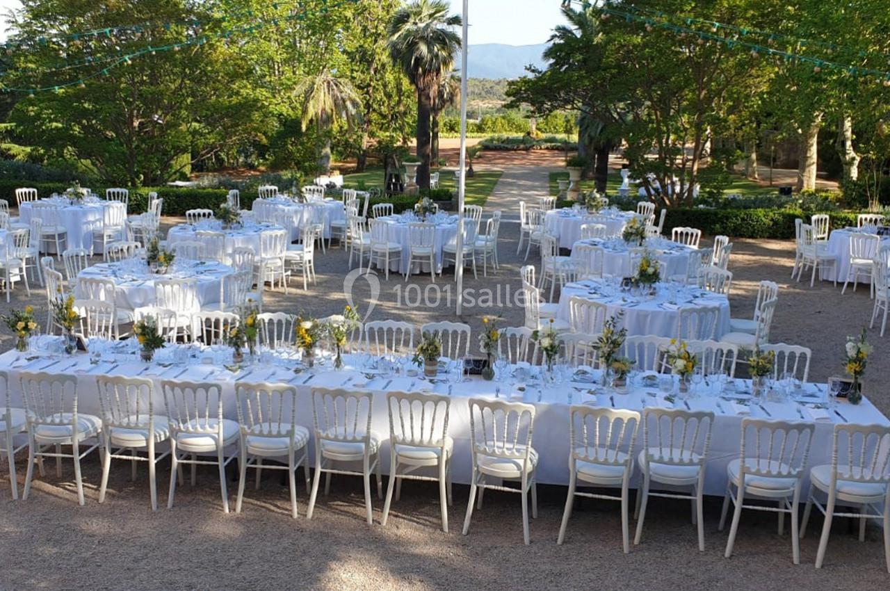 Tables dressées pour un événement en plein air, avec nappes blanches, chaises alignées et décorations florales.