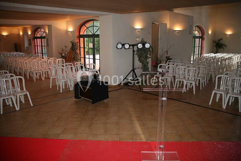 Salle lumineuse aménagée avec des rangées de chaises blanches, un pupitre transparent et un éclairage de scène.