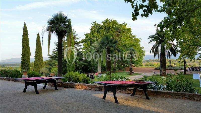 Deux tables noires avec nappes rouges sur une terrasse gravillonnée, entourées de palmiers et de végétation.
