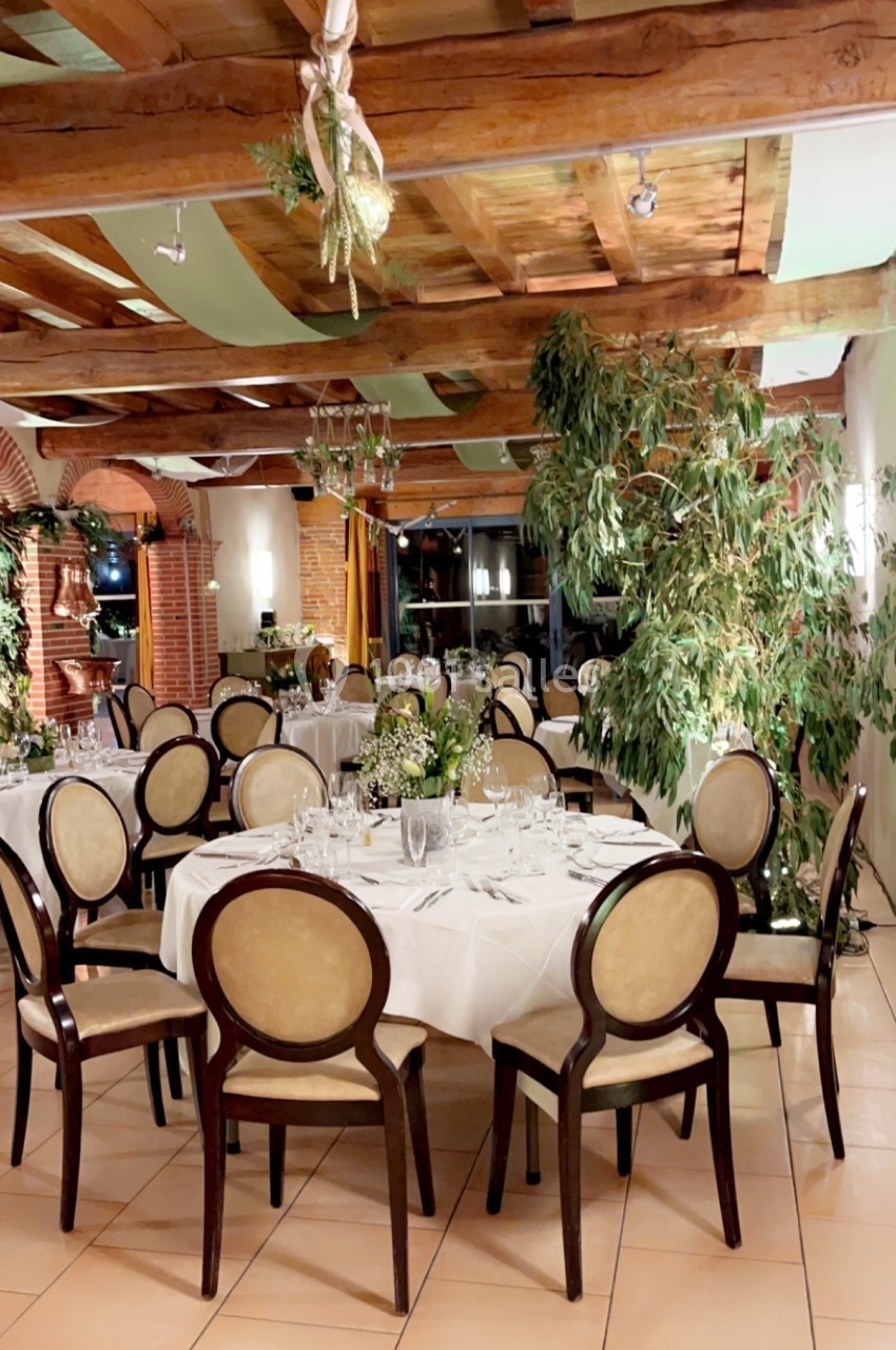 Salle de réception élégante avec tables rondes dressées, chaises classiques et décoration végétale abondante.