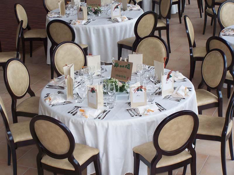 Salle de réception avec tables rondes dressées, nappes blanches, chaises rembourrées et décorations de table élégantes.