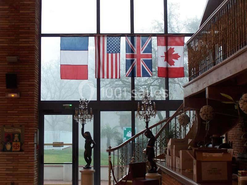 Quatre drapeaux (France, États-Unis, Royaume-Uni, Canada) suspendus devant une grande baie vitrée dans un hall.