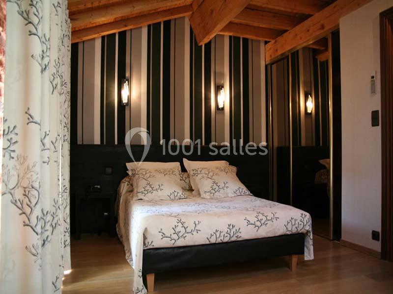 Chambre avec lit double, plafond en bois, murs à rayures noires et blanches, et rideaux à motifs végétaux.