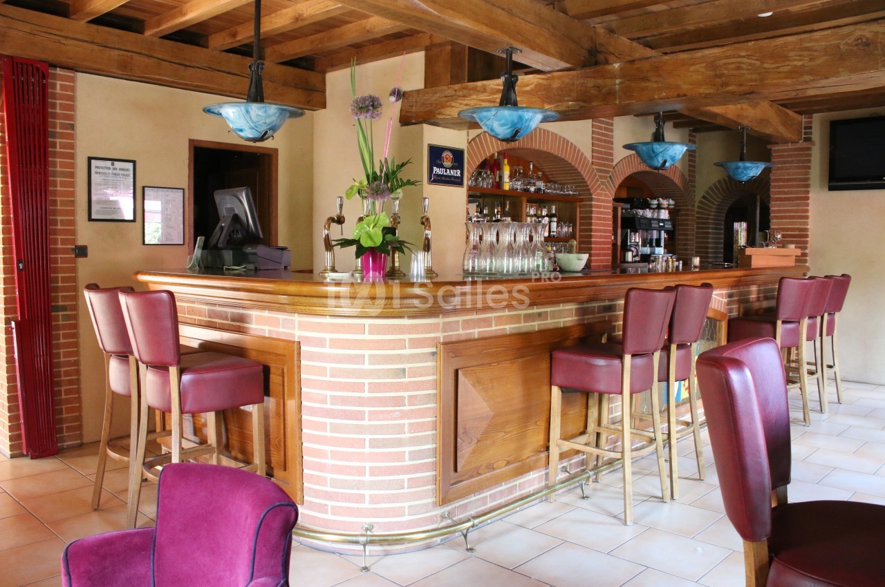 Bar en bois avec comptoir en briques, tabourets rouges, décorations florales et luminaires suspendus.