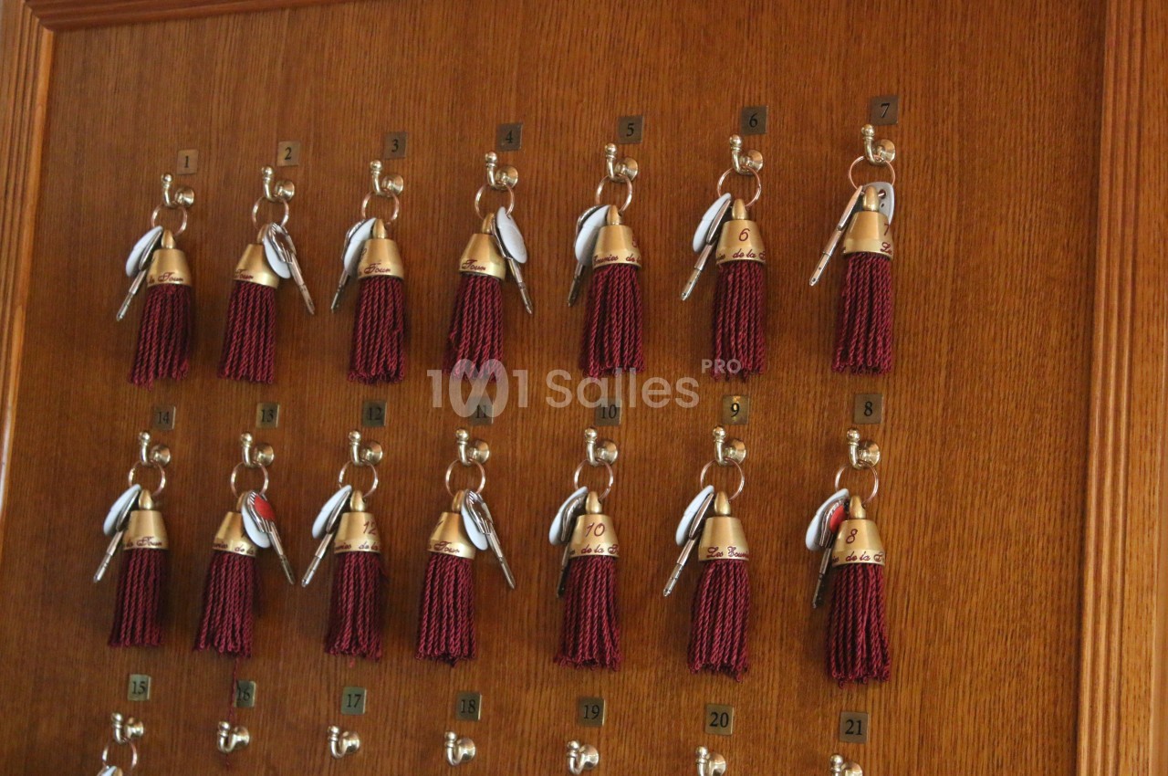 Clés d'hôtel avec porte-clés à pompons rouges accrochées sur un tableau en bois numéroté.