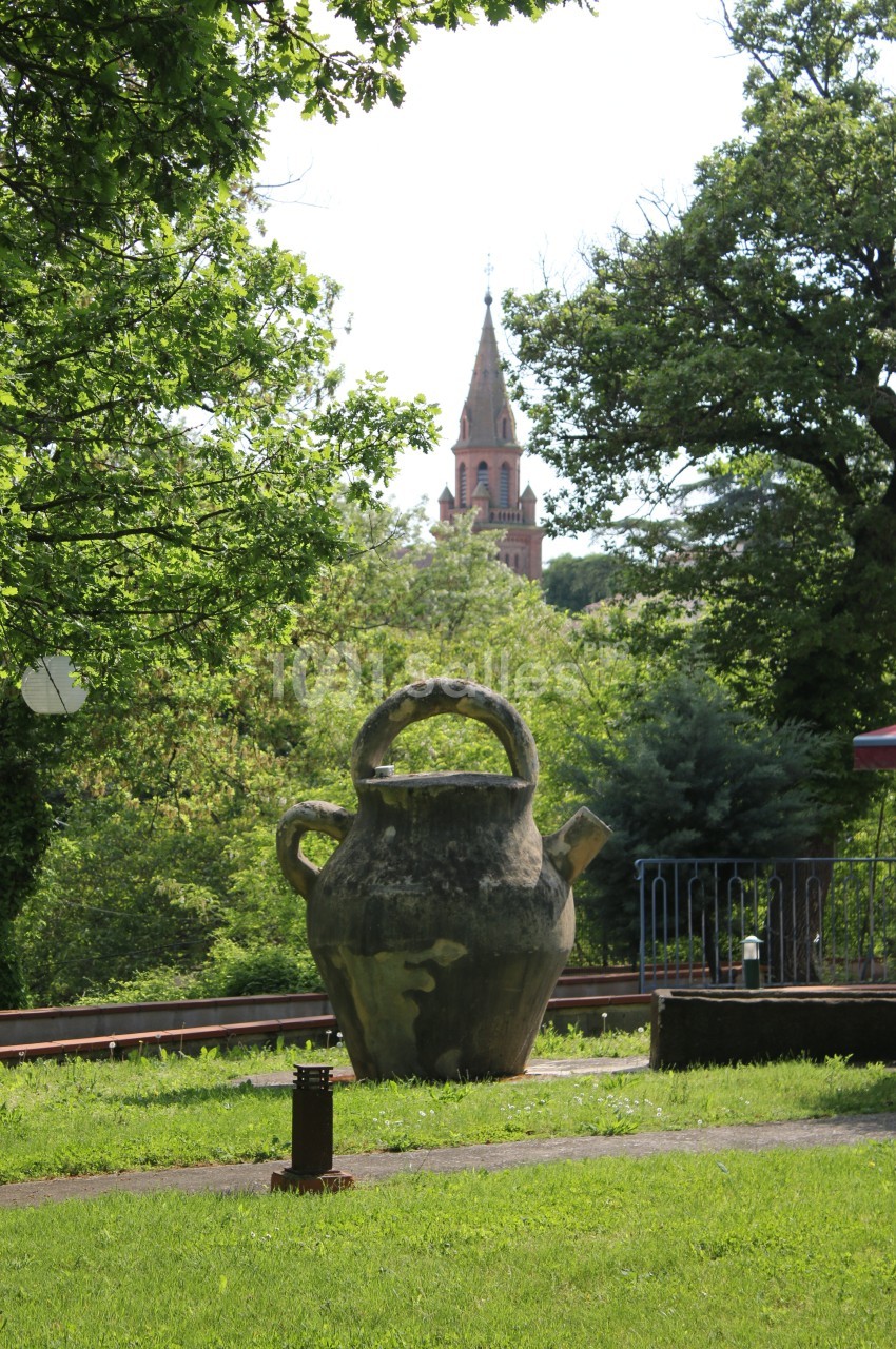 Grande jarre en pierre dans un parc verdoyant, avec une église en arrière-plan sous un ciel clair.