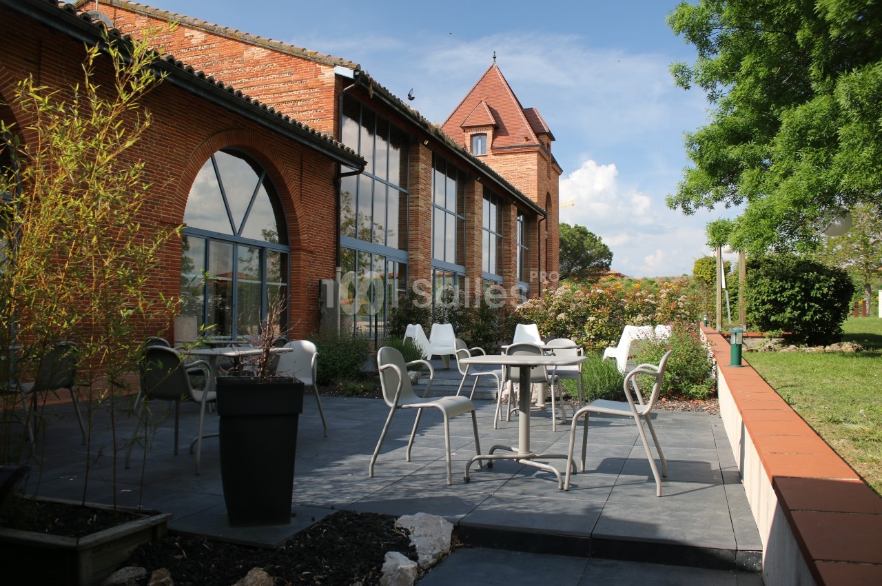 Terrasse extérieure avec tables et chaises devant un bâtiment en briques rouges, entourée de végétation.