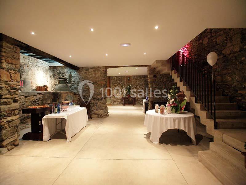Salle en pierre avec éclairage chaleureux, tables dressées pour un buffet et escalier en pierre sur la droite.