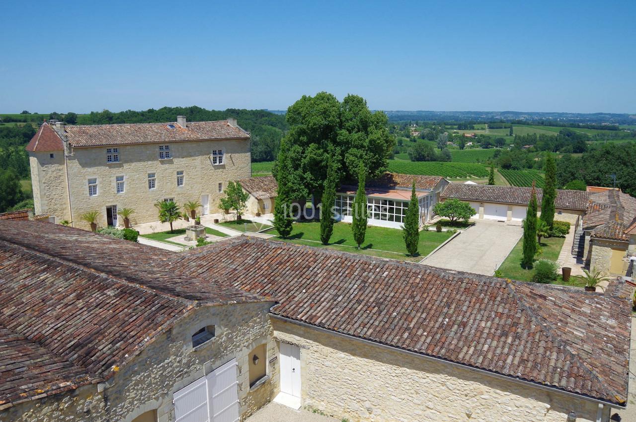 Vue aérienne d'un domaine avec bâtiments en pierre, toits en tuiles, cour centrale et paysage rural en arrière-plan.