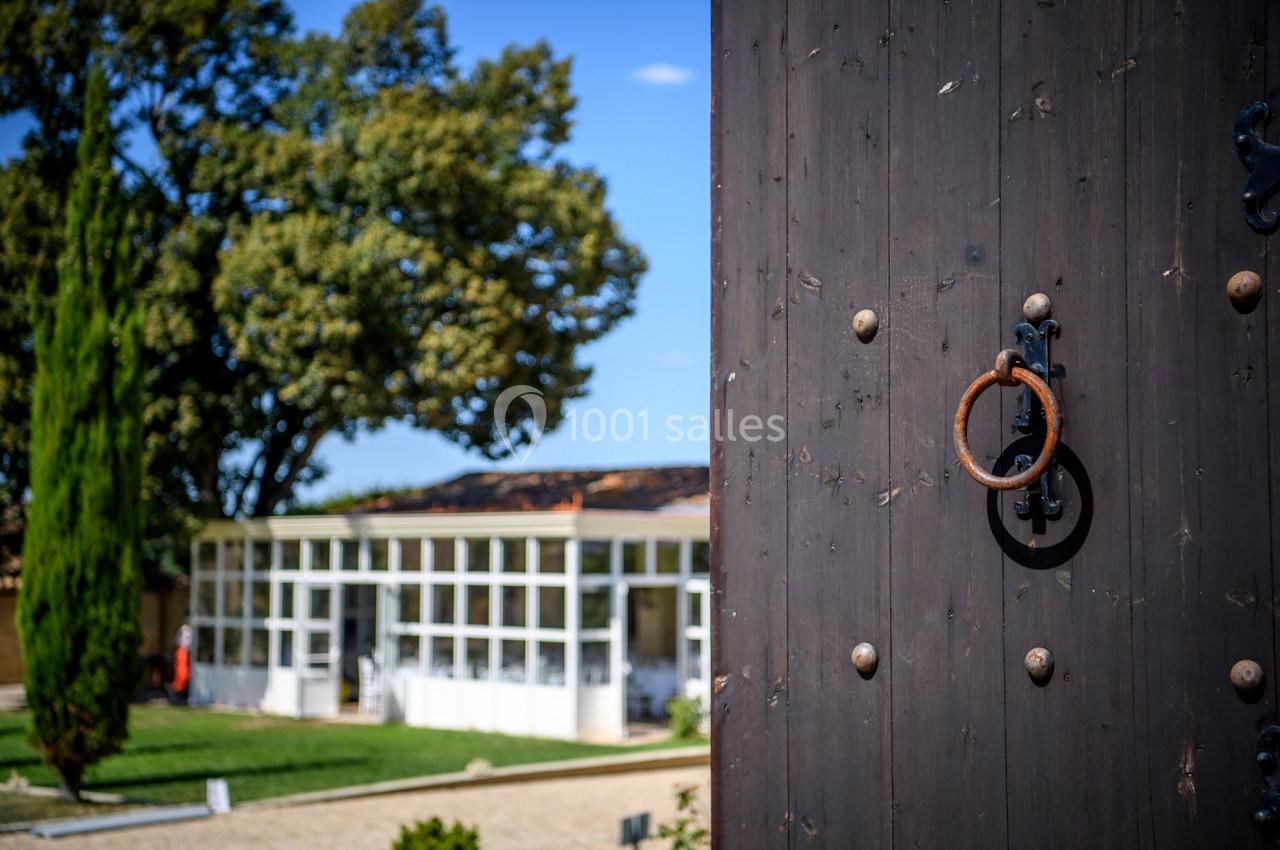 Porte en bois sombre avec heurtoir en métal, donnant sur un jardin avec arbres et bâtiment vitré en arrière-plan.