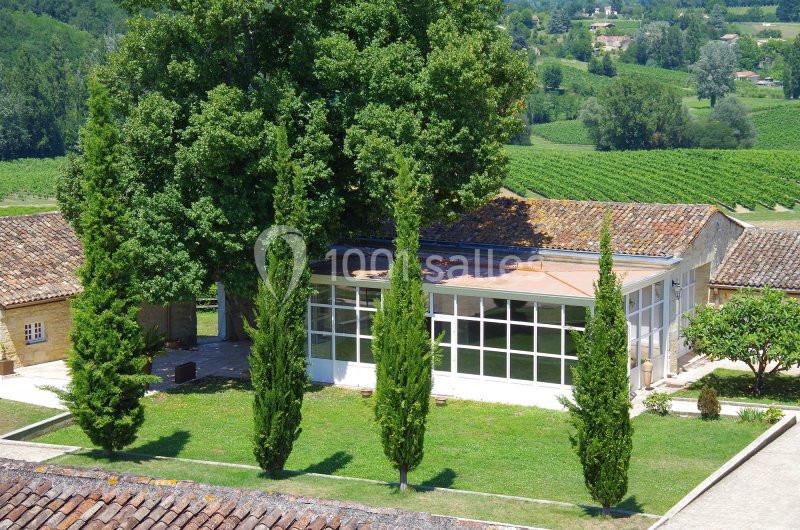 Bâtiment moderne avec façade vitrée entouré de cyprès et d'arbres, situé dans un paysage rural verdoyant.