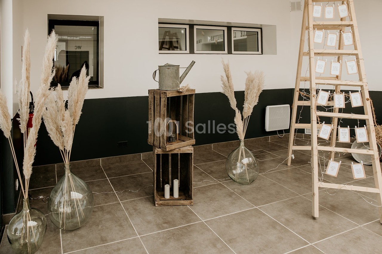 Décoration intérieure avec échelle en bois portant des cartes, vases de pampas et caisses en bois sur un sol carrelé.