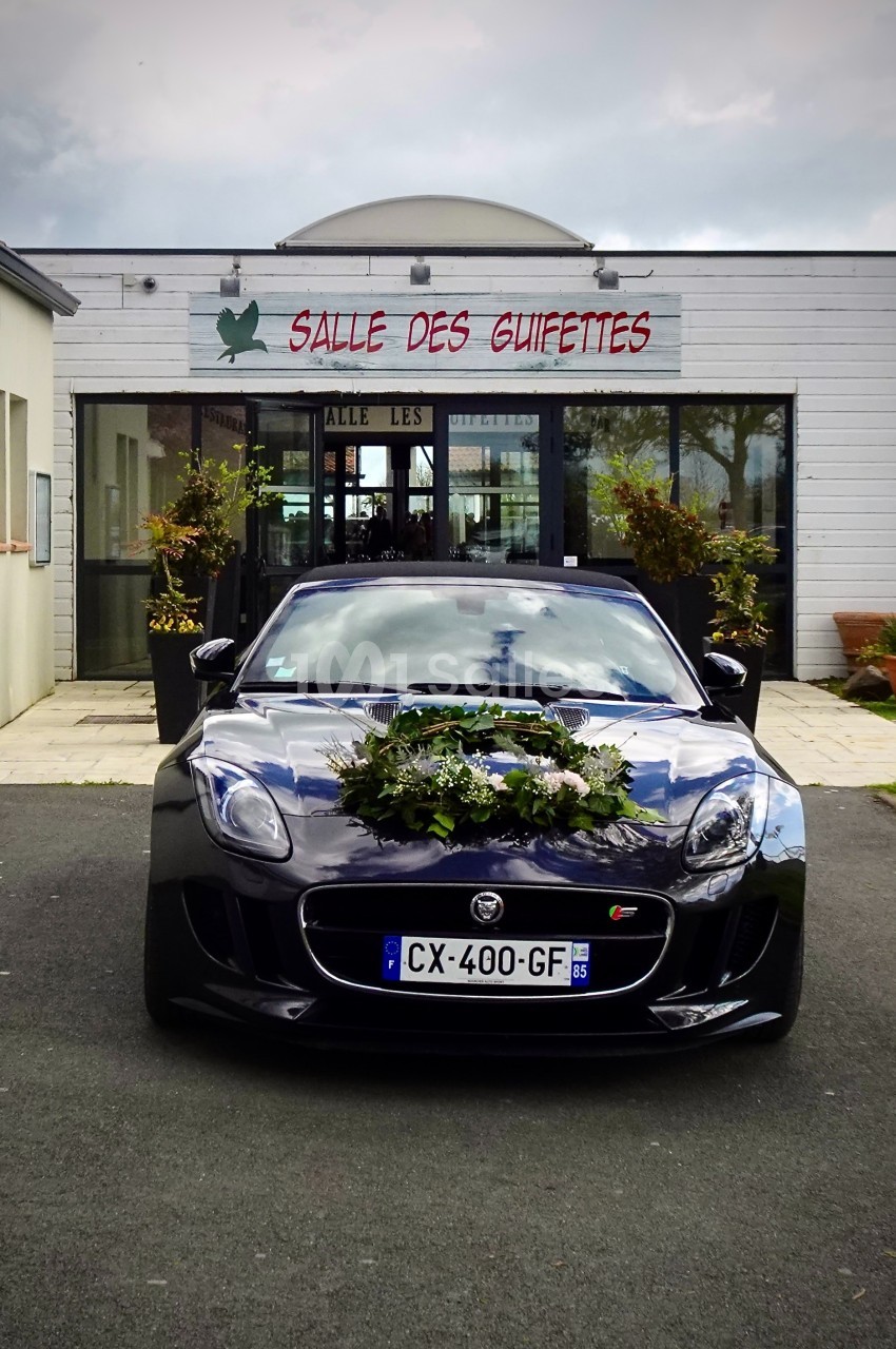 Voiture noire décorée de fleurs devant une salle de réception avec enseigne ’Salle des Guifettes’.