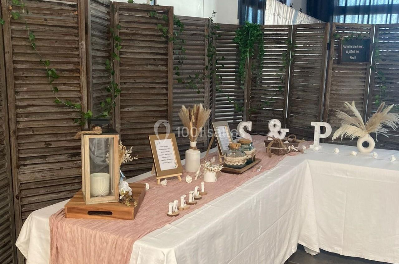 Table décorative avec nappe rose, bougies, cadres, fleurs séchées et lettres décoratives devant un paravent en bois.