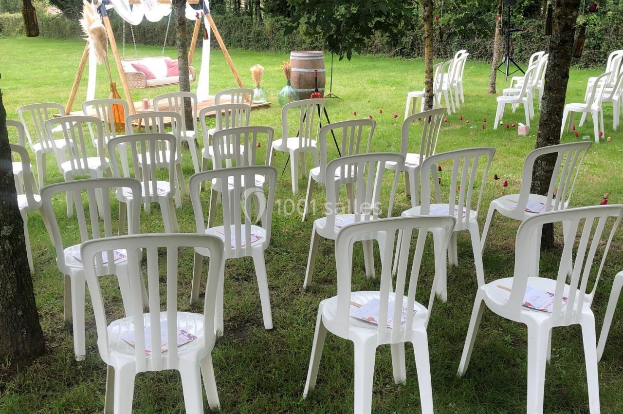 CEREMONIE LAIQUE Chaises blanches en plastique disposées en rangées sur une pelouse, face à une arche décorée pour une cérémonie en plein air.