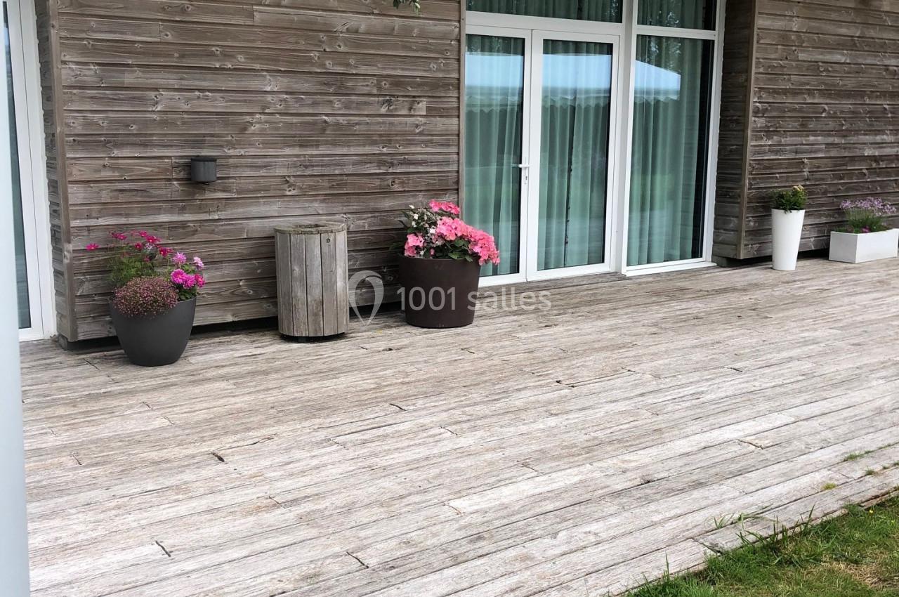 L'ESPACE DU LAC Terrasse en bois avec pots de fleurs, pergola en bois et grandes baies vitrées donnant sur l'intérieur.
