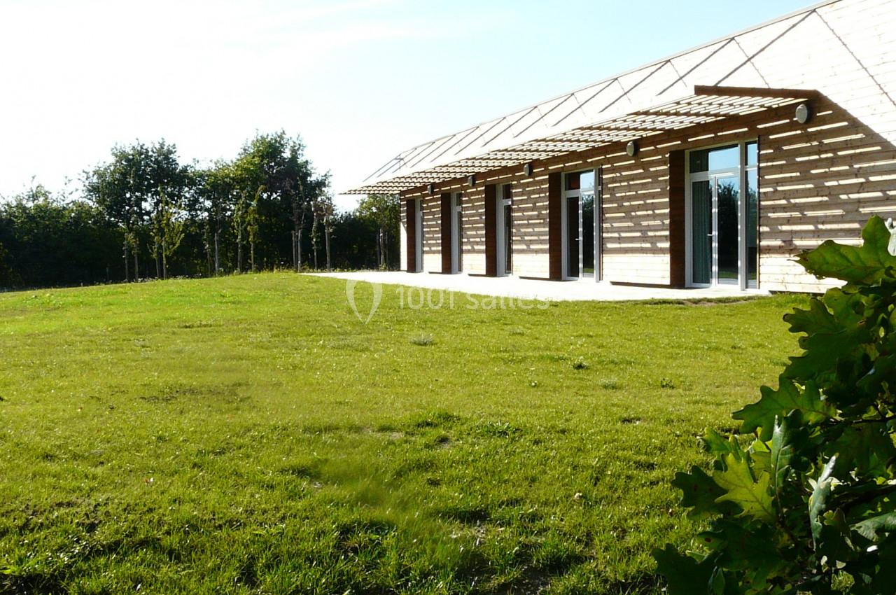 L'ESPACE DU LAC Bâtiment en bois avec de grandes baies vitrées, entouré d'une pelouse et d'arbres sous un ciel dégagé.