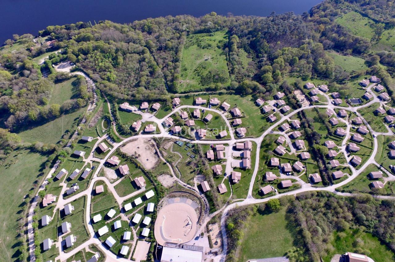 Le Domaine du pré Vue aérienne d'un village avec des maisons dispersées, entouré de verdure et bordé par un cours d'eau.