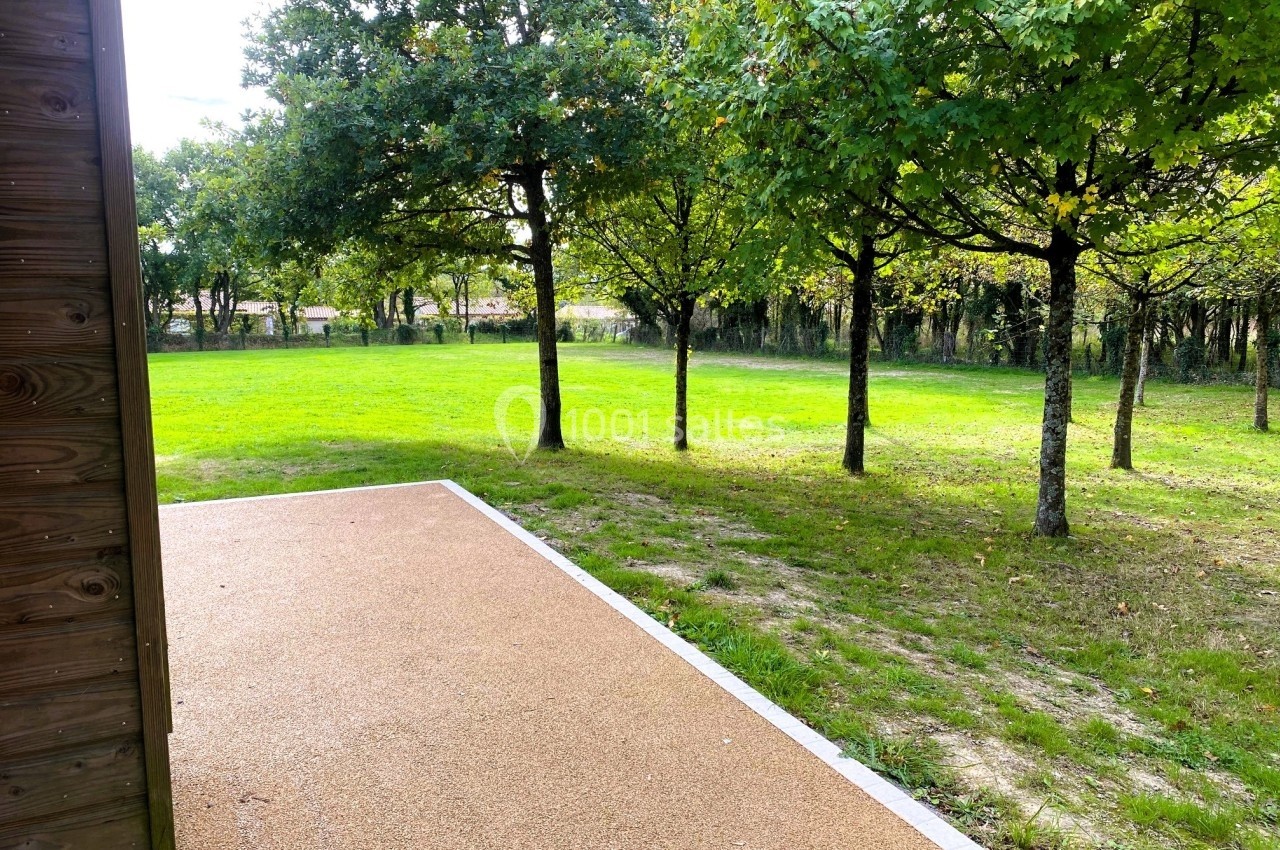 NOUVELLE TERRASSE Allée en gravier beige bordée d'herbe, donnant sur un espace vert avec des arbres sous un ciel clair.