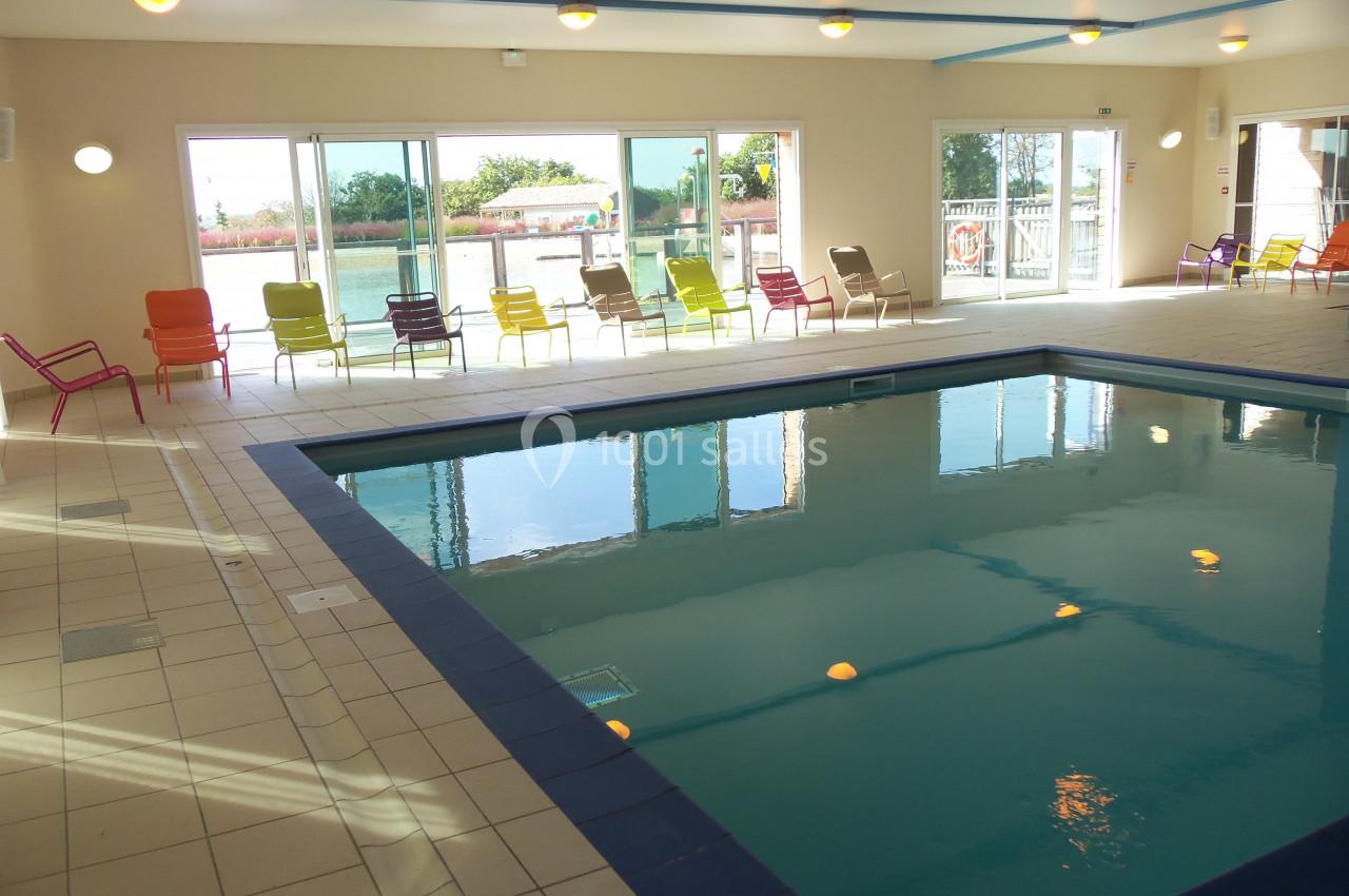 PISCINE INTERIEURE Piscine intérieure lumineuse avec chaises colorées alignées près des baies vitrées donnant sur un espace extérieur.
