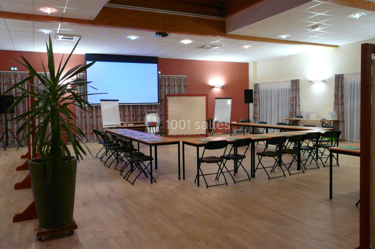 SALLE BELLEVUE SEMINAIRE Salle de réunion équipée de tables en U, chaises, projecteur, écrans et plantes décoratives.