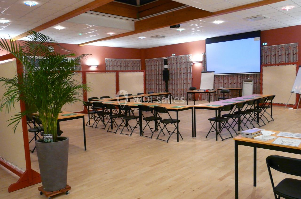 SALLE BELLEVUE SEMINAIRE Salle de réunion avec tables disposées en U, chaises pliantes, écran de projection et plantes décoratives.