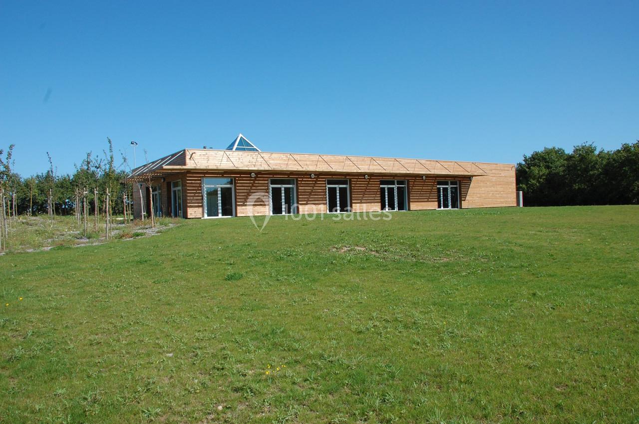 SALLE DE RECEPTION Bâtiment en bois à un étage avec de grandes baies vitrées, entouré d'une pelouse et d'arbres sous un ciel bleu.