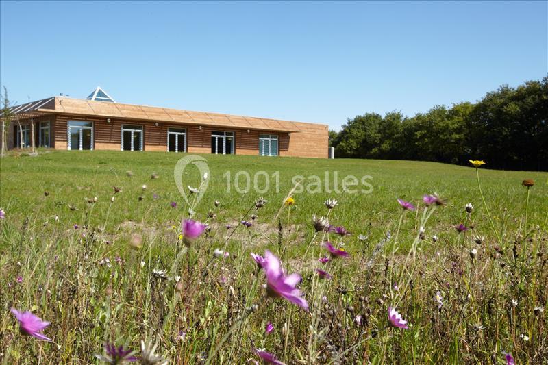 SALLE ESPACE DU LAC, VUE DE L'EXTERIEUR Bâtiment en bois moderne entouré d'une prairie fleurie et d'une pelouse sous un ciel bleu.