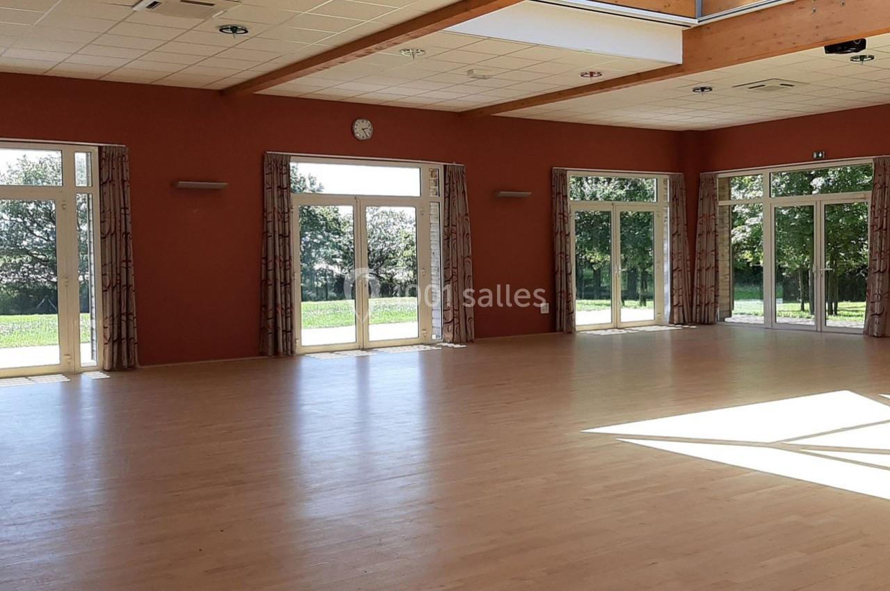 SALLE LE JAUNAY Salle lumineuse avec parquet clair, grandes baies vitrées donnant sur un espace extérieur verdoyant.