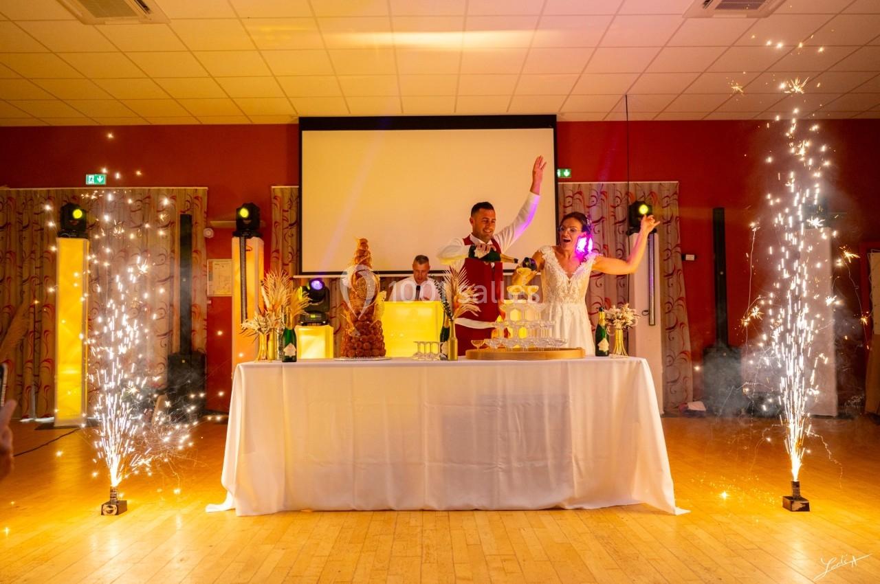 SALLE LE JAUNAY Un couple debout derrière une table décorée, entouré de fontaines d'étincelles dans une salle de réception.