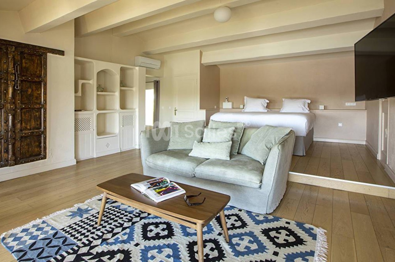 Salon lumineux avec canapé, table basse, tapis à motifs, et lit en arrière-plan dans une pièce au décor épuré.