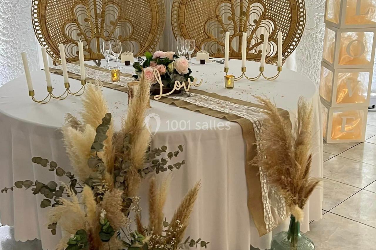 Table décorée pour un événement avec chandeliers, fleurs séchées, nappes blanches et chaises en rotin sculpté.