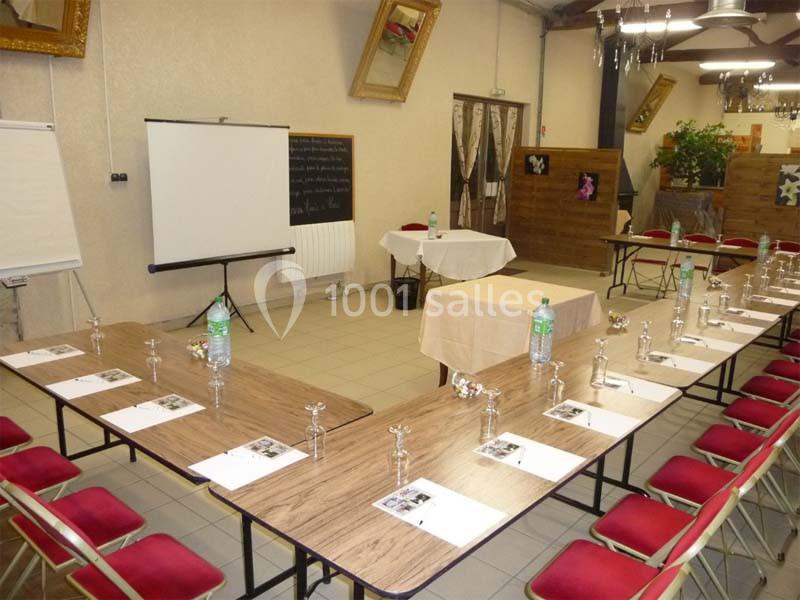 Salle de réunion aménagée en U avec tables, chaises rouges, documents, bouteilles d'eau et matériel de présentation.
