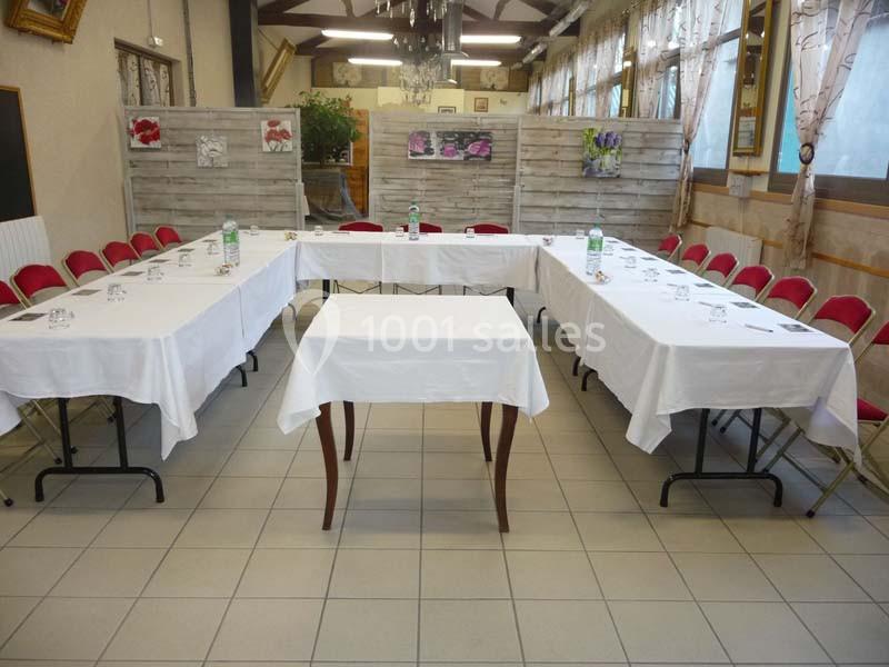 Salle aménagée en U avec des tables recouvertes de nappes blanches, entourées de chaises rouges.
