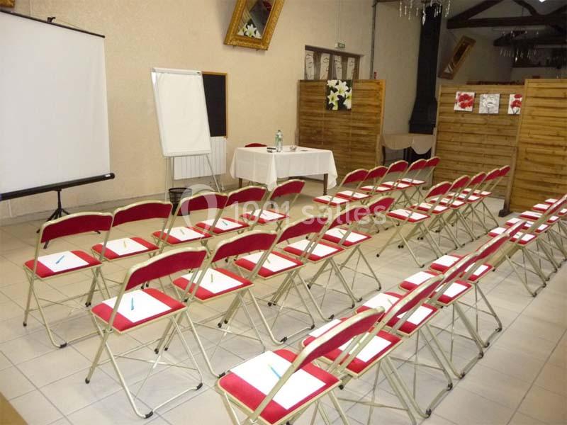 Salle aménagée pour une réunion avec des chaises alignées, un tableau blanc, un écran de projection et une table.