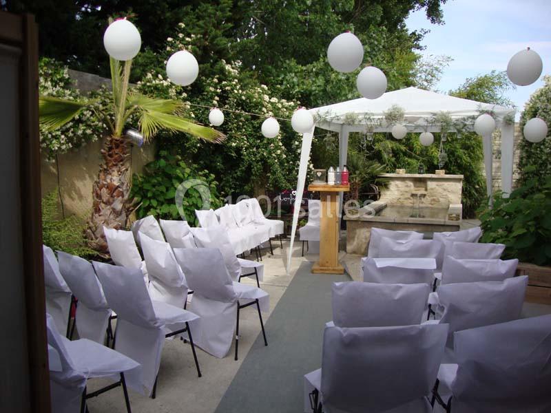 Chaises blanches alignées sous une tonnelle décorée de lanternes, dans un jardin verdoyant.
