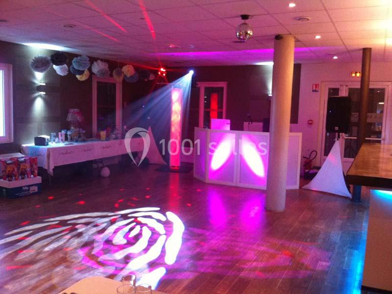 Salle de réception avec éclairage coloré, piste de danse, table décorée et espace DJ éclairé.