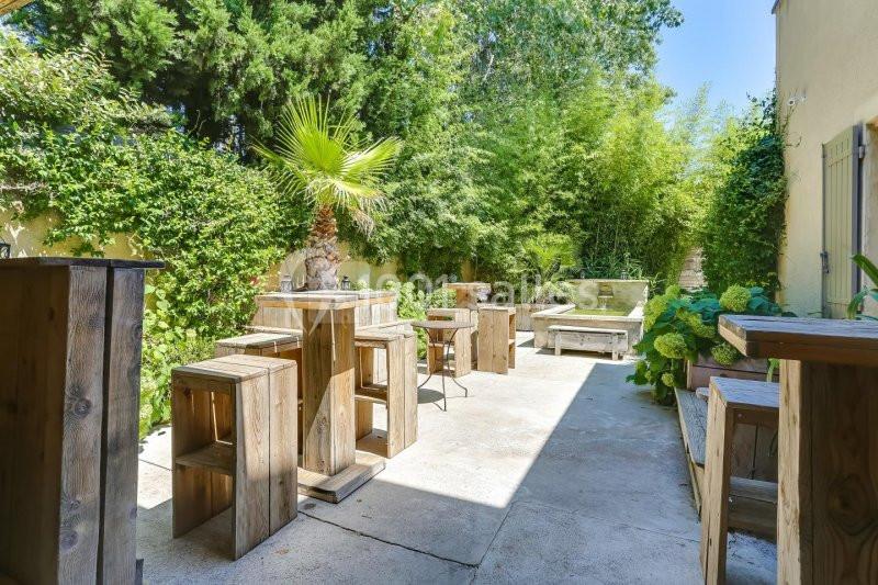 Terrasse extérieure avec tables et tabourets en bois, entourée de végétation dense et d'un bassin décoratif.