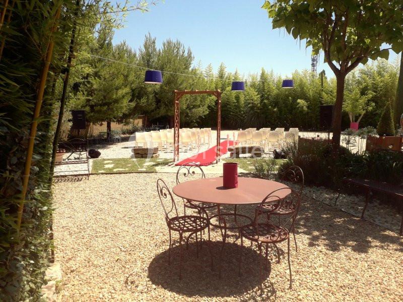 Espace extérieur aménagé pour une cérémonie, avec chaises alignées, tapis rouge et table en fer forgé au premier plan.