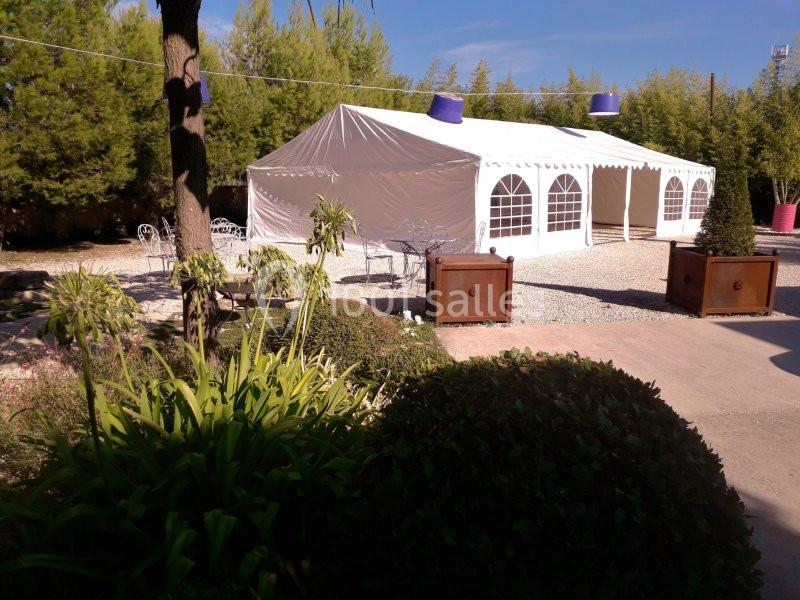 Tente blanche installée dans un jardin avec des plantes, des arbres et du mobilier de jardin en arrière-plan.