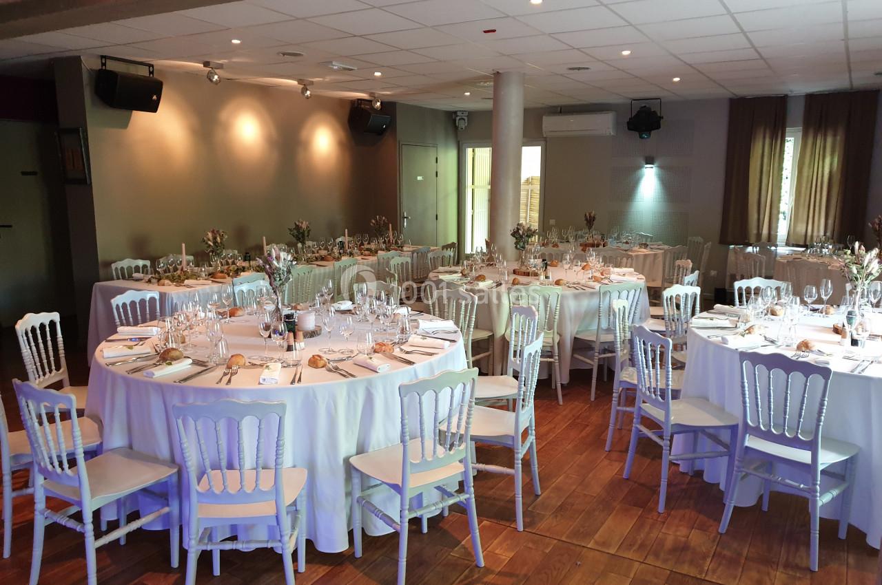 Salle de réception décorée avec des tables rondes dressées, nappes blanches et chaises élégantes sur un parquet en bois.