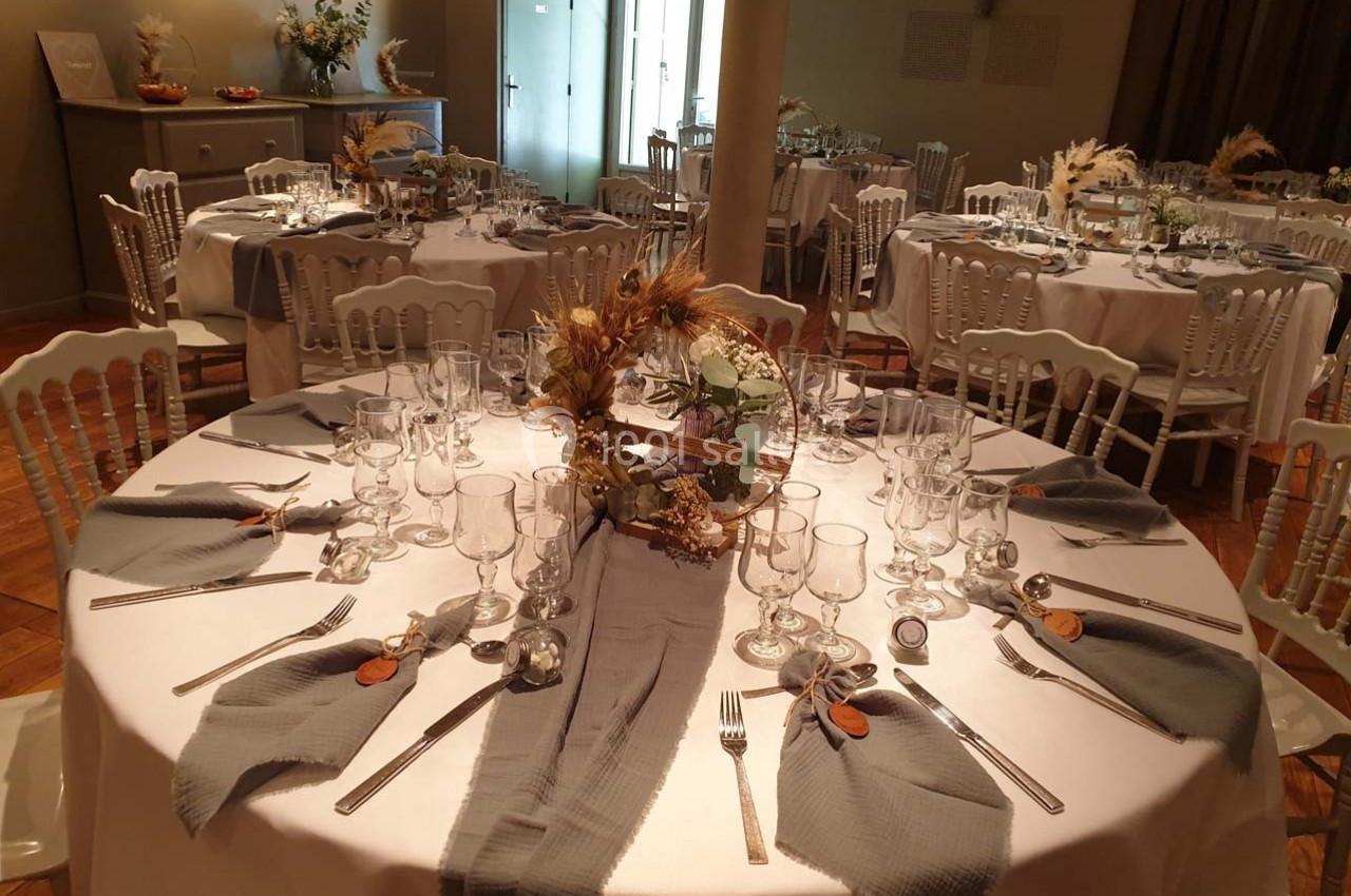 Table ronde élégamment dressée avec nappes blanches, serviettes grises et centre de table floral dans une salle de réception.