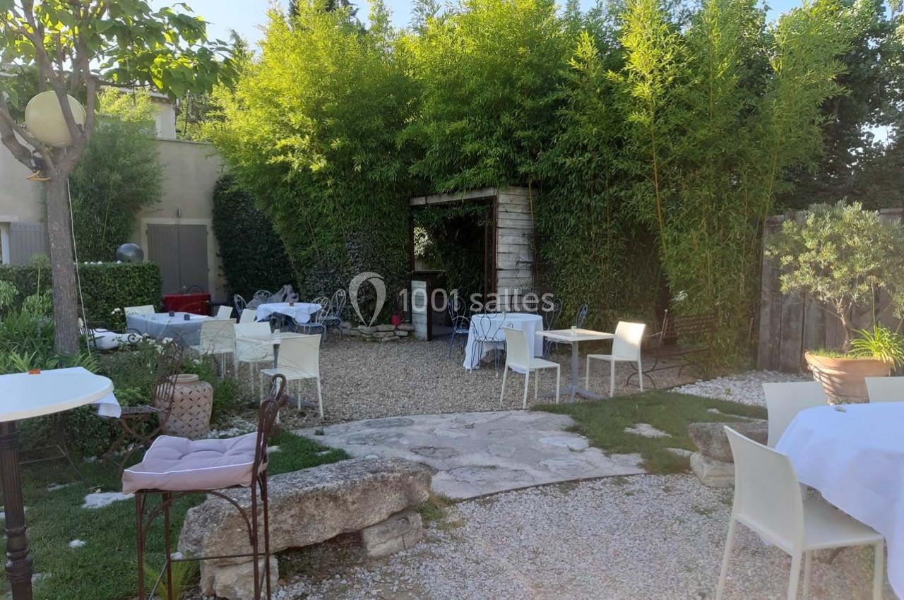 Jardin avec tables et chaises blanches disposées sur du gravier, entouré de bambous et de verdure.