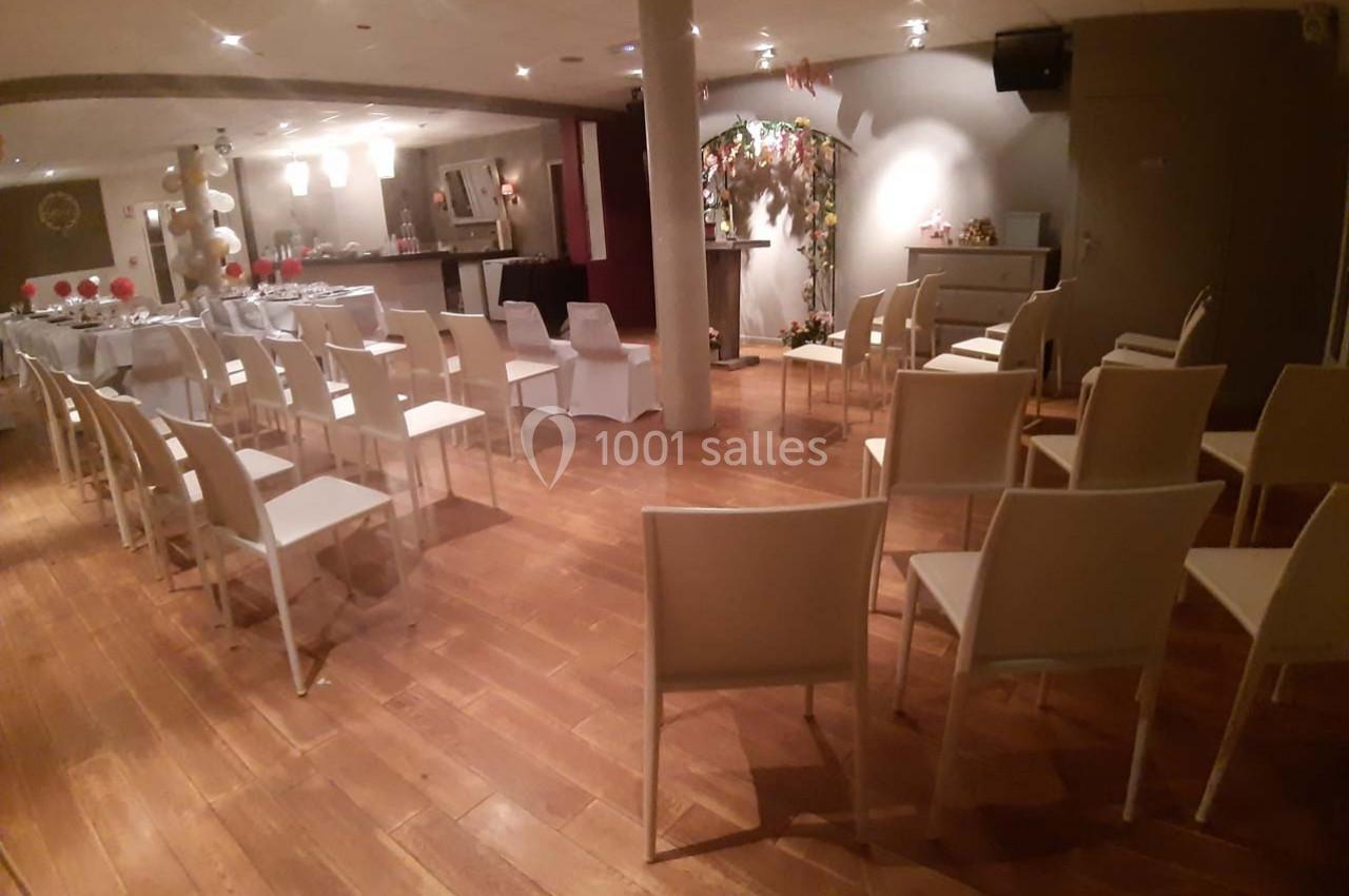 Salle aménagée avec des chaises blanches alignées, un espace décoré et une table en fond pour un événement.
