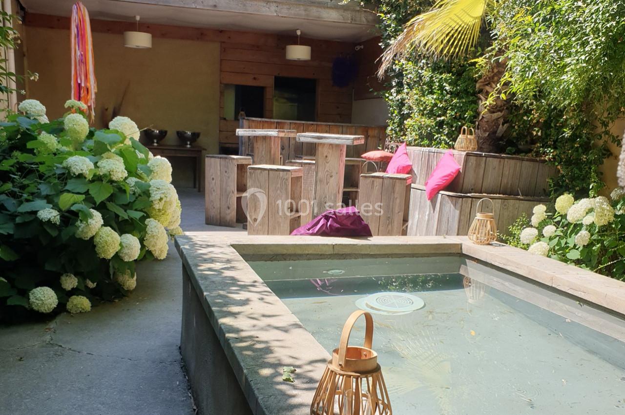 Espace extérieur avec bassin peu profond, mobilier en bois, coussins colorés et végétation luxuriante.