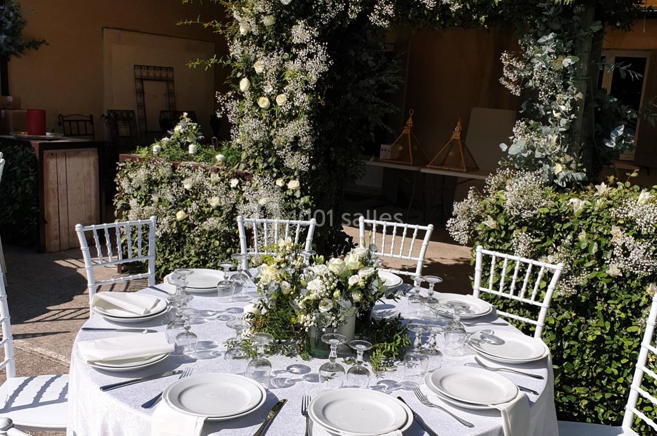 Table ronde décorée pour un événement, avec nappes blanches, vaisselle élégante et centre de table floral.